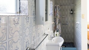 A bathroom with patterned tiles, a white sink, a mirror, and a shower area. - Rustic, cosy one bedroom guesthouse. Just a short walk to Umina Beach! (Umina Beach)