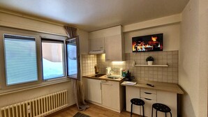 Ett litet kök med ett fönster, ett element, en diskho och två pallar.