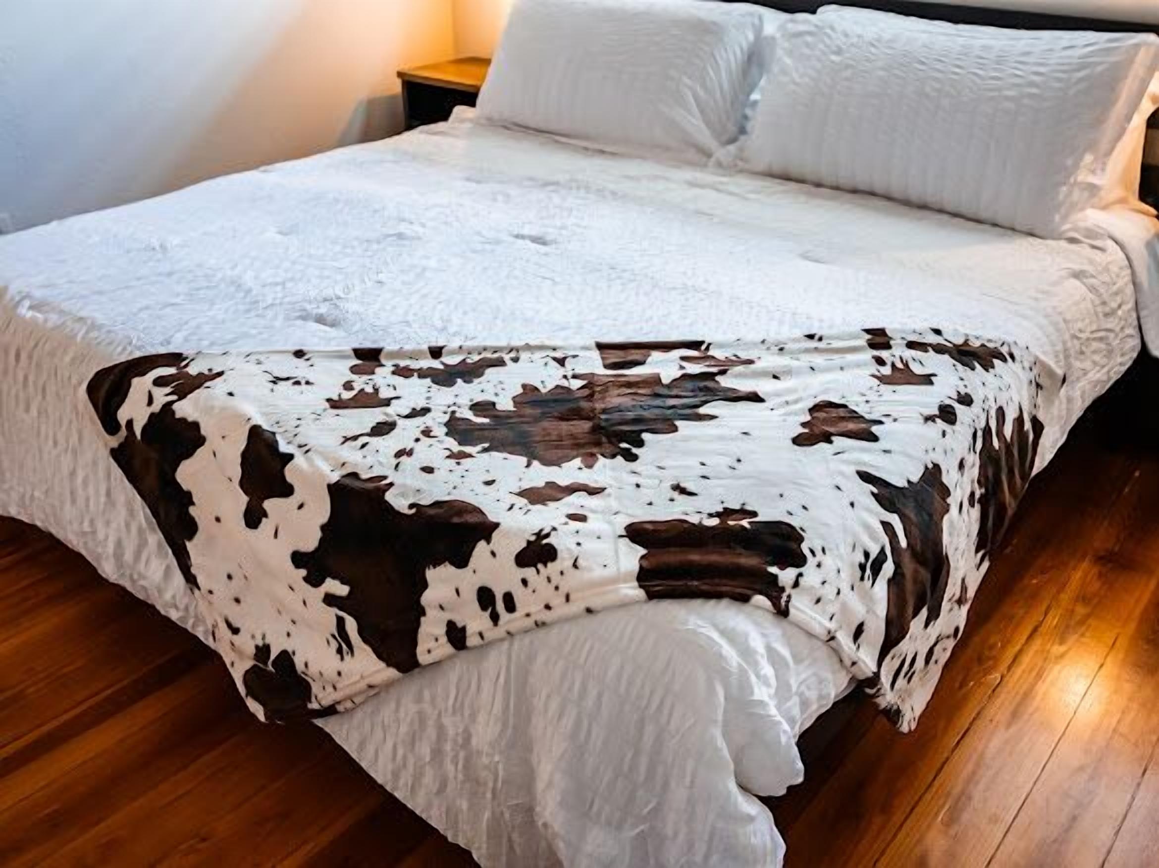 A bed with a white quilt and a cow print blanket.