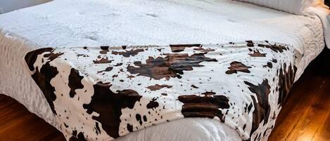 A bed with a white quilt and a cow print blanket.