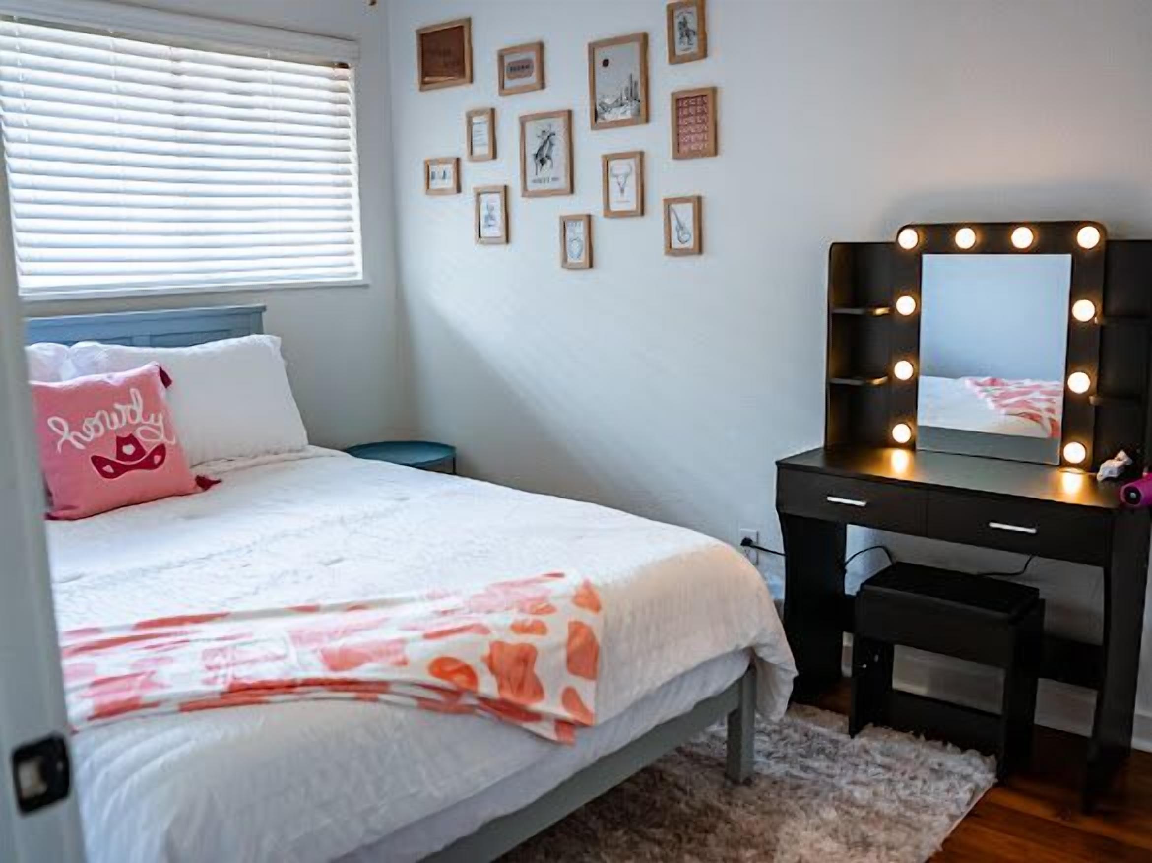 A bedroom with a bed, a vanity with lights, and framed pictures on the wall.