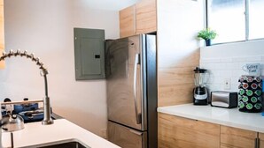 Una cocina moderna con armarios de madera, un refrigerador de acero inoxidable, horno empotrado, un lavamanos, cafetera y licuadora.