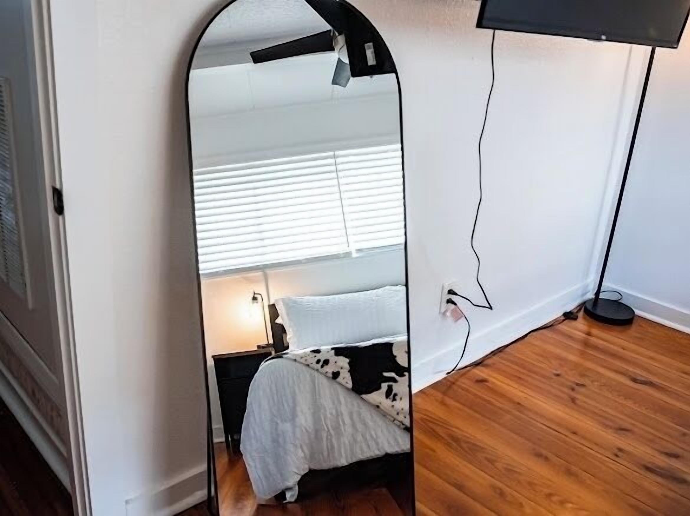A bedroom with a bed, a bedside table, a lamp, and a mirror reflecting the room.
