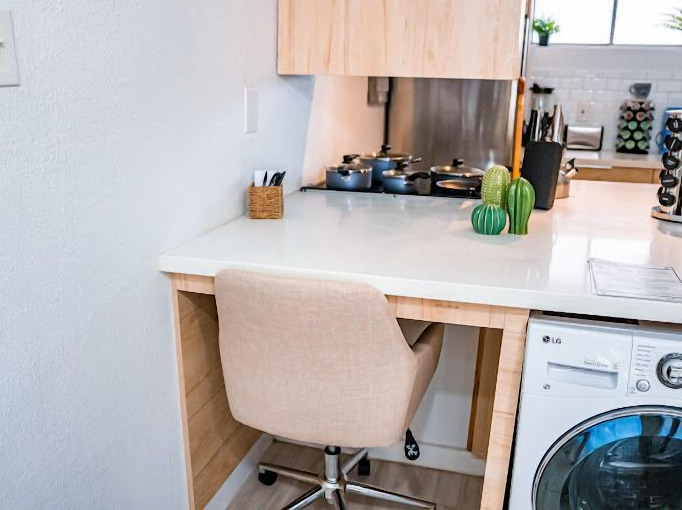 A compact kitchen with a white countertop, a built-in stove, a washing machine, and a chair.