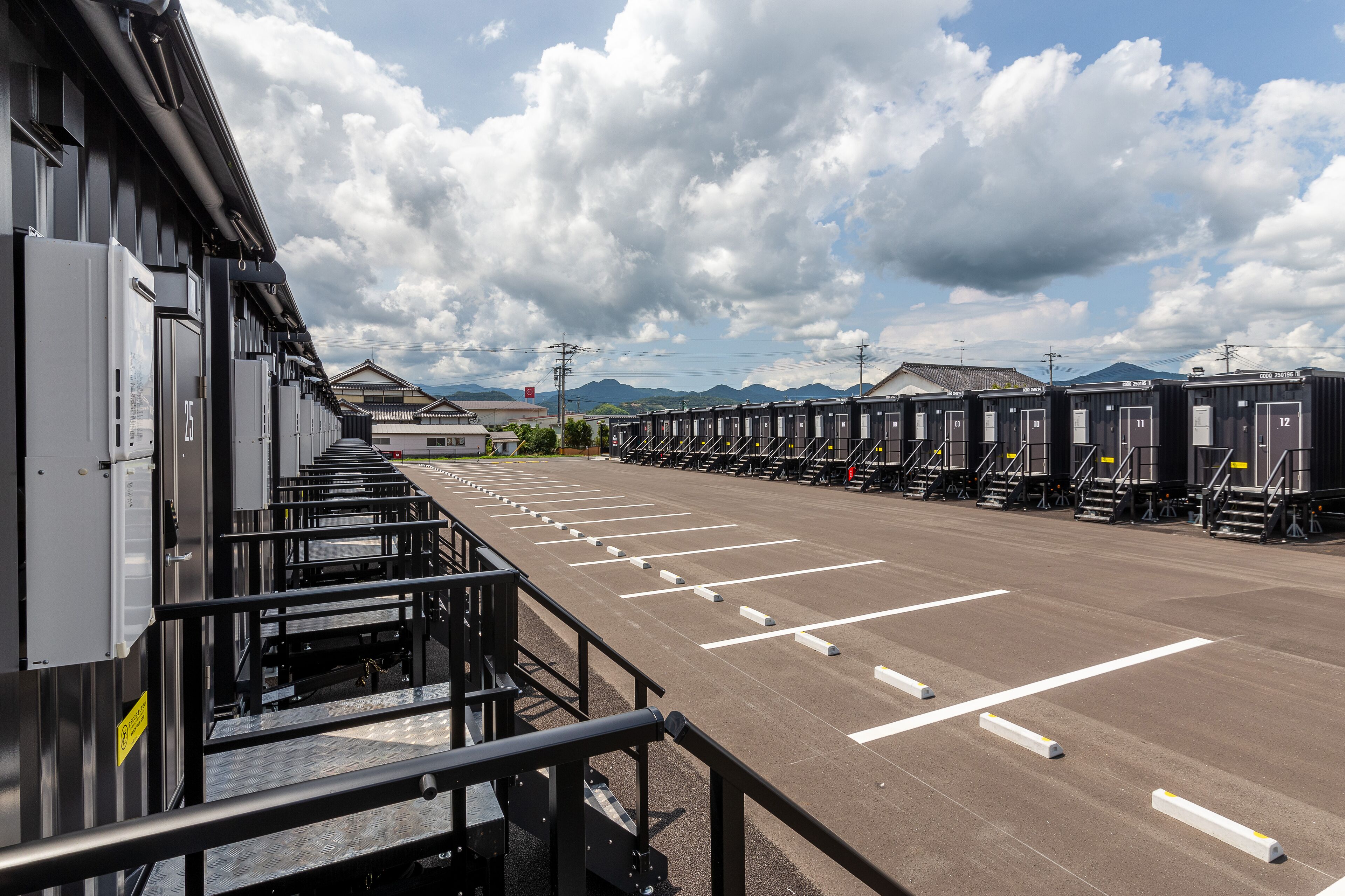A row of portable cabins with numbered doors, a parking area, and a building with a metal facade.