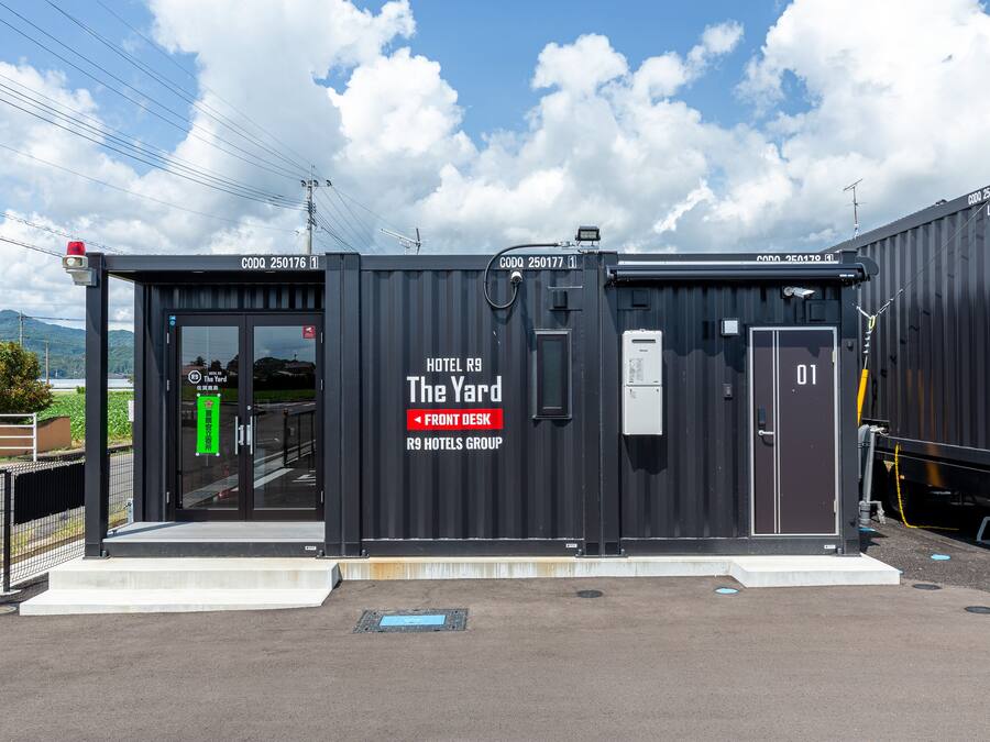 Un edificio tipo contenedor de color negro con el rótulo "The Yard", y la señalización "R9 Hotels Group" y "Recepción".