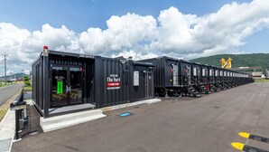 A row of black modular hotel units with a sign reading "HOTELS The Yard" and "R9 Hotels Group".