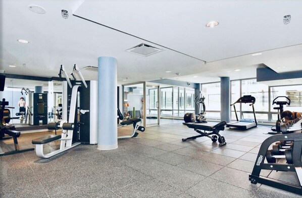 A modern gym with various exercise equipment, large windows, and a spacious layout.