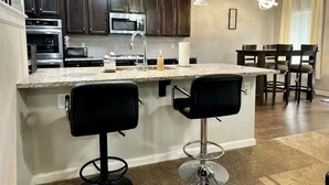 Una cucina moderna con mobili scuri, elettrodomestici in acciaio inossidabile, un piano di lavoro in granito e due sgabelli neri.