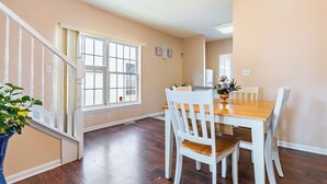 A dining area with a wooden table and white chairs, a staircase with white railings, and a large window with curtains. - Only 8 min to Ohio State University! (Columbus)