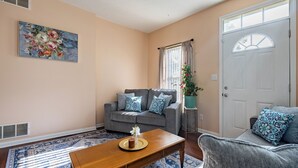 A living room with a sofa, a coffee table, a painting, and a door. - Only 8 min to Ohio State University! (Columbus)