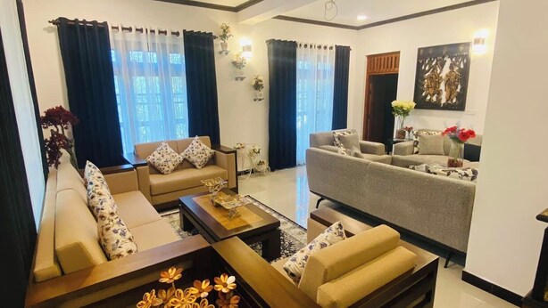 A spacious living room with a sofa set, a coffee table, and a dining area with a table and chairs. - Hotel White House (Halloluwa)