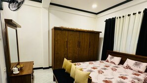 A bedroom with a bed, bedside table, mirror, wardrobe, and a ceiling fan. - Hotel White House (Halloluwa)