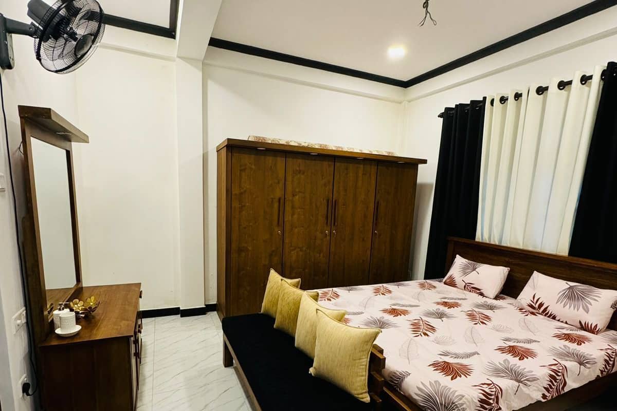 Ein Schlafzimmer mit Bett, Nachttisch, Spiegel, Kleiderschrank und Deckenventilator.
