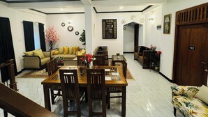 A spacious living area with a dining table, sofas, and a wooden door marked with the number 102. - Hotel White House (Halloluwa)