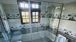 A modern bathroom with a glass-enclosed shower, two sinks, and a toilet. - Hotel White House (Halloluwa)