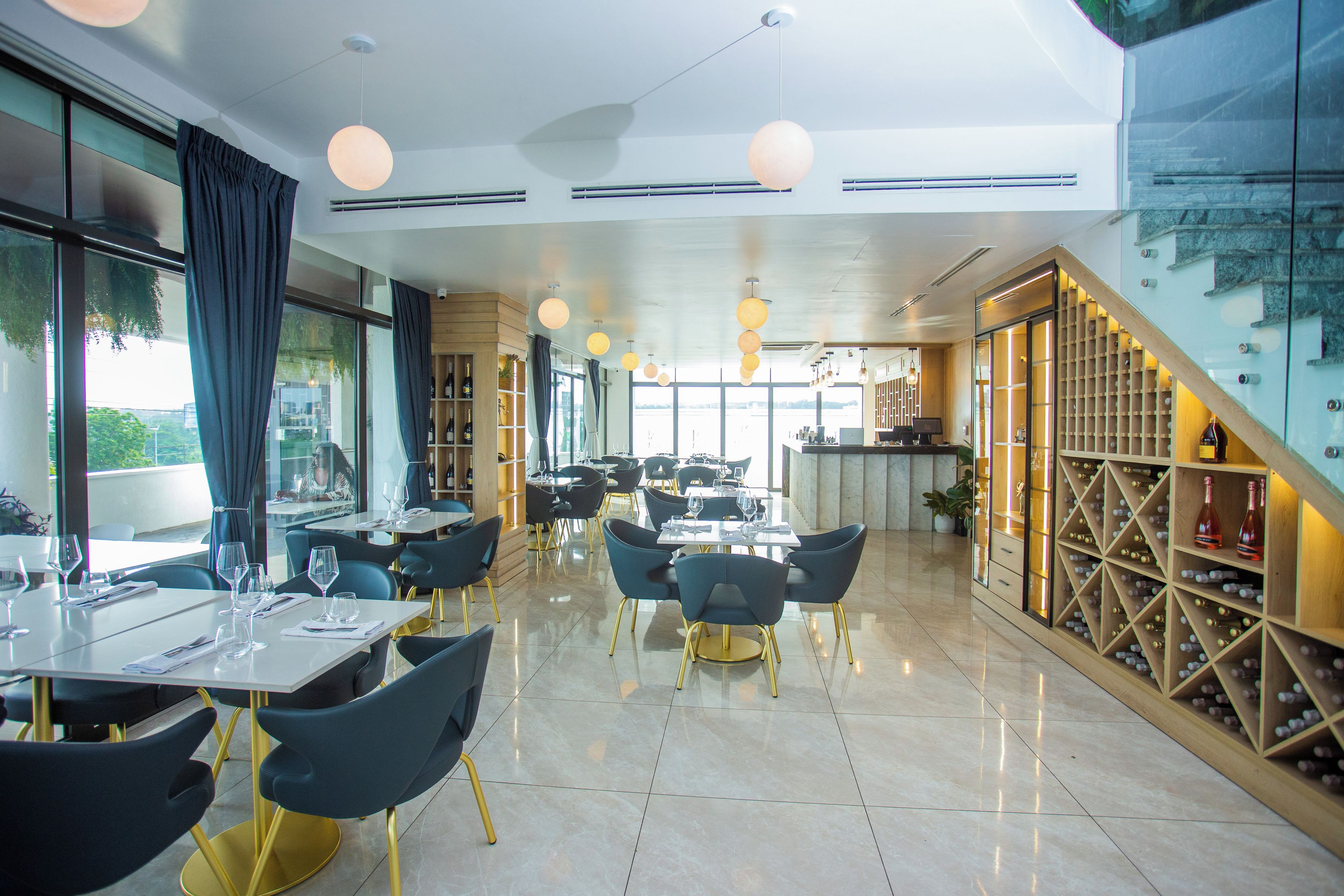 A modern restaurant interior with tables, chairs, and a wine rack.