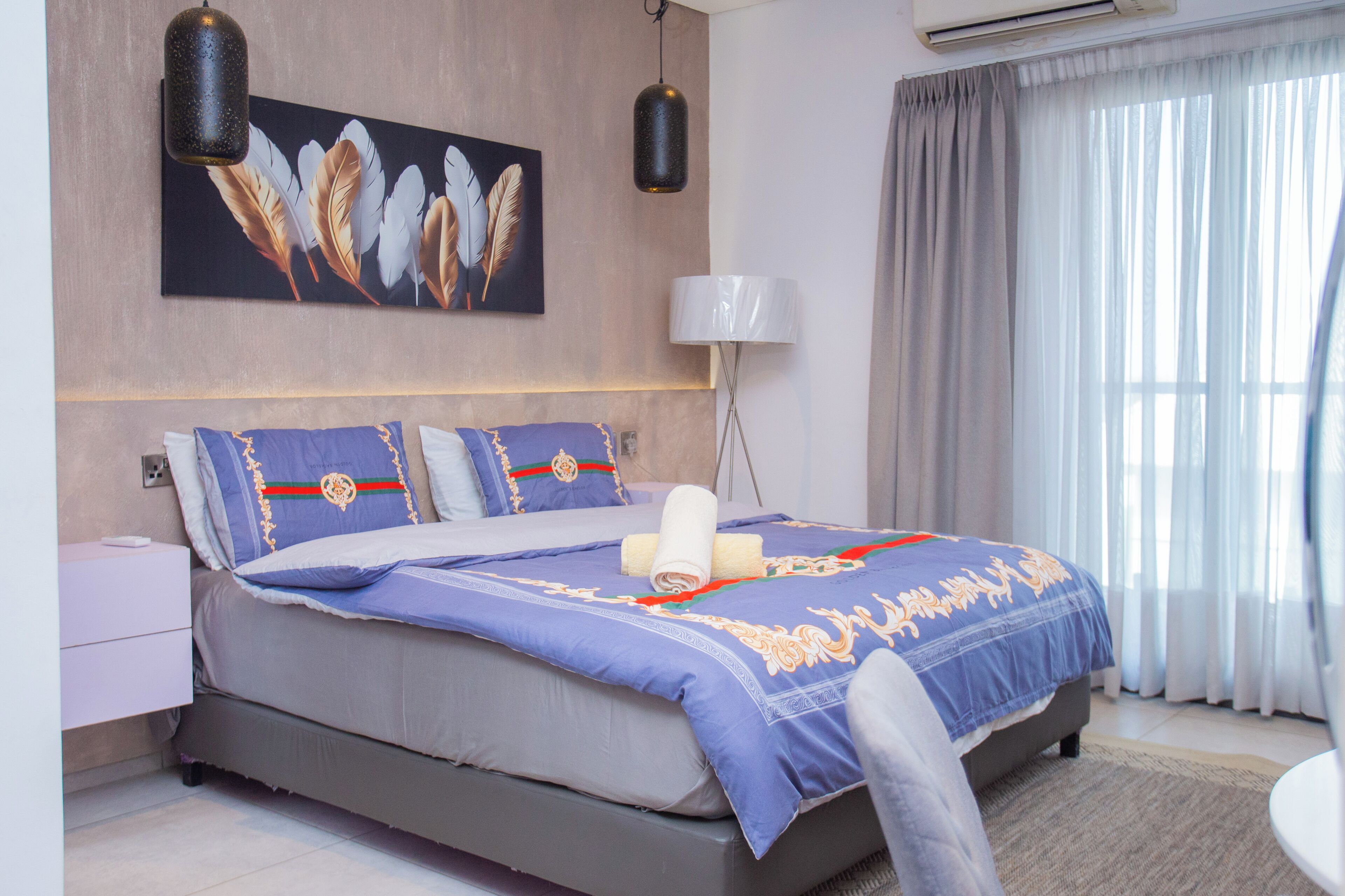Un dormitorio moderno con una cama grande, aire acondicionado de pared, una lámpara de noche y una ventana con cortinas.