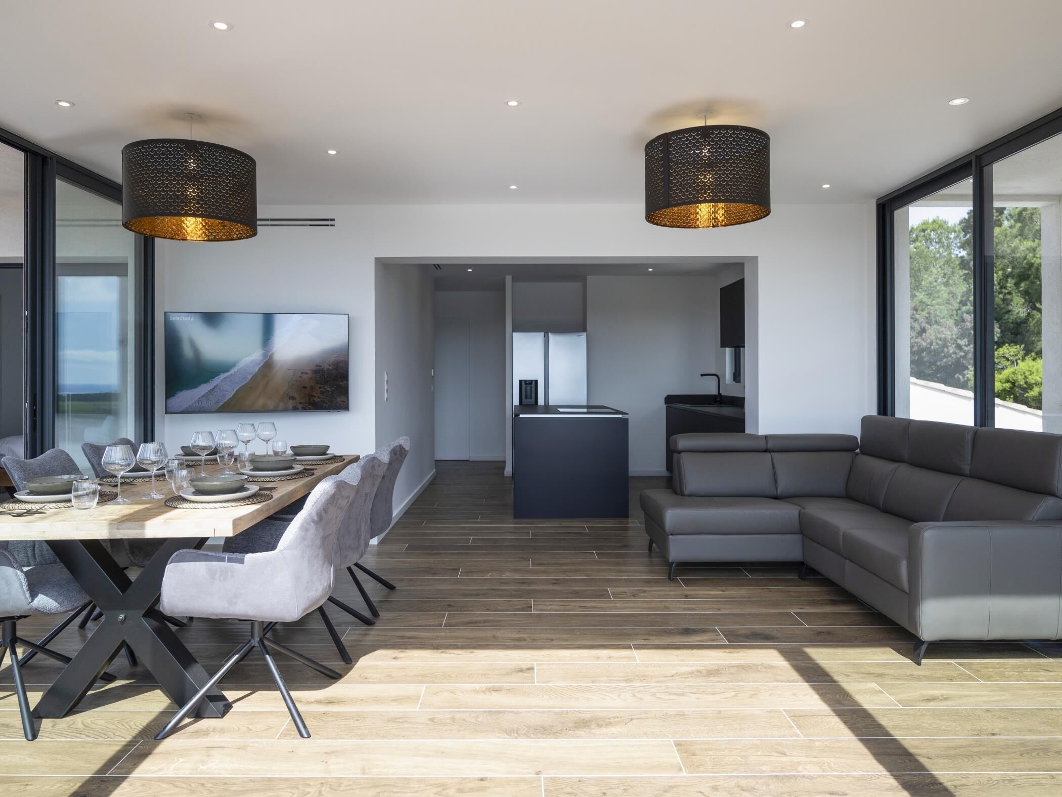 A modern living room with a dining area, a kitchen, and a large window offering a view of the outdoors.