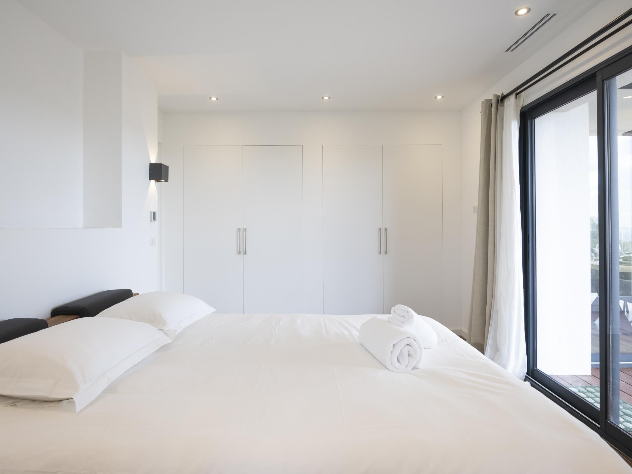 A modern hotel room with a large bed, a wardrobe, and a view through a large window.