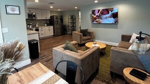 A modern living room with a sofa, coffee table, and TV. There is a kitchen in the background with appliances and cabinets. - Inland Escape - Centrally Located (Jacksonville)