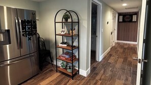 A kitchen with a stainless steel refrigerator, a black metal shelf with decorative items, and wooden flooring. - Inland Escape - Centrally Located (Jacksonville)