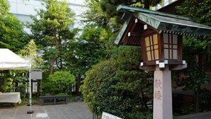 Il s’agit d’une lanterne japonaise traditionnelle, dotée d’une base en bois et d’un toit vert, qui se trouve dans un jardin agrémenté d’un banc en pierre et, au fond, d’une tente blanche.