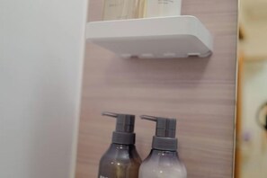 Une salle de bain avec une étagère blanche au-dessus d’un miroir, deux flacons de savon liquide et un mur en bois.