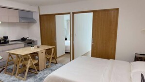 Une chambre d’hôtel compacte, dotée d’une kitchenette, d’un lit avec du linge de lit blanc et d’un bureau en bois avec des chaises.