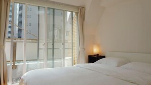 Une chambre d’hôtel dotée d’une grande porte-fenêtre coulissante, d’un lit avec du linge de lit blanc et d’une lampe de chevet.