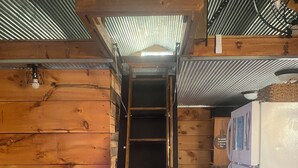 Un interior de madera con una escalera de madera central que lleva a un altillo, un refrigerador y un sofá.