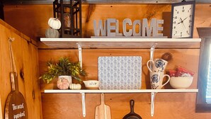 Cocina con armarios de madera, estufa y diversos utensilios de cocina. Un letrero con la palabra 'WELCOME' está sobre la encimera.