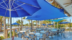 An outdoor dining area with tables and chairs, umbrellas, and a pool in the background. - OV 1035 Golf Course and Ocean View -Welcome to Paradise (Fort Pierce)