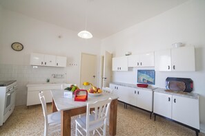 A kitchen with white cabinets, a dining table with chairs, a clock on the wall, and a microwave on the countertop.