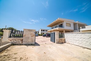 A modern residential building with a gated entrance, paved driveway, and a clear blue sky.
