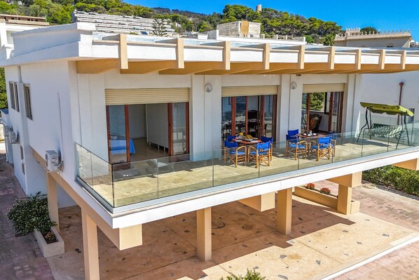 A modern building with a glass balcony, outdoor seating, and a view of the surrounding area.