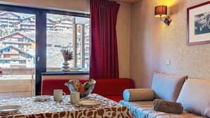 Ein gemütliches Zimmer mit Esstisch für zwei Personen, einer Couch, einem Fenster mit Blick auf Gebäude und einer Wandleuchte.