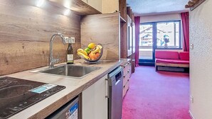 Eine moderne Küche mit Spüle aus Edelstahl, integriertem Backofen und Geschirrspüler. Auf der Arbeitsfläche steht eine Obstschale und ein Fenster bietet Blick ins Freie.