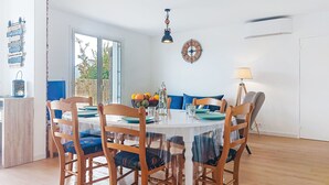 Een eetgedeelte met een ronde tafel, houten stoelen en een blauw kussen. Een klok en een lamp hangen aan de muur.