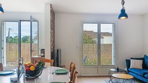 Een eetruimte met een tafel voor vier personen, een blauwe bank en een uitzicht op een achtertuin door glazen deuren.