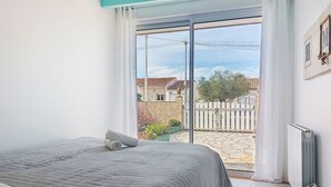 Een slaapkamer met een groot bed, een radiator en uitzicht op een binnentuin met een witte schutting en groen.
