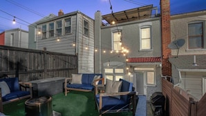 Un patio con mobiliario exterior, luces colgantes y una chimenea.