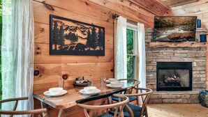 A wooden cabin interior with a dining table set for four, a fireplace, and a forest scene artwork. - Ever & After Cabin (Pigeon Forge)