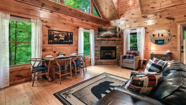 A cozy cabin interior with a dining area, fireplace, and a large window overlooking greenery. - Ever & After Cabin (Pigeon Forge)