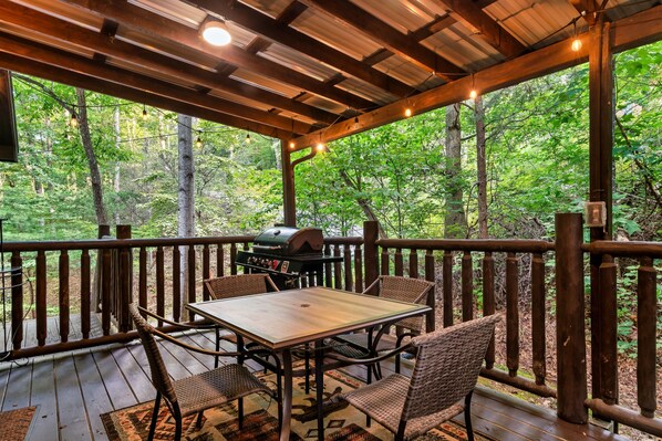 A wooden deck with a table and chairs, surrounded by a wooden railing, overlooking a forested area.