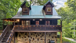 A rustic cabin with a stone foundation, a wooden deck, and a metal roof. - Ever & After Cabin (Pigeon Forge)