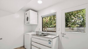 Une cuisine compacte équipée d’un lave-linge intégré, d’un évier et d’une fenêtre donnant sur un espace verdoyant.