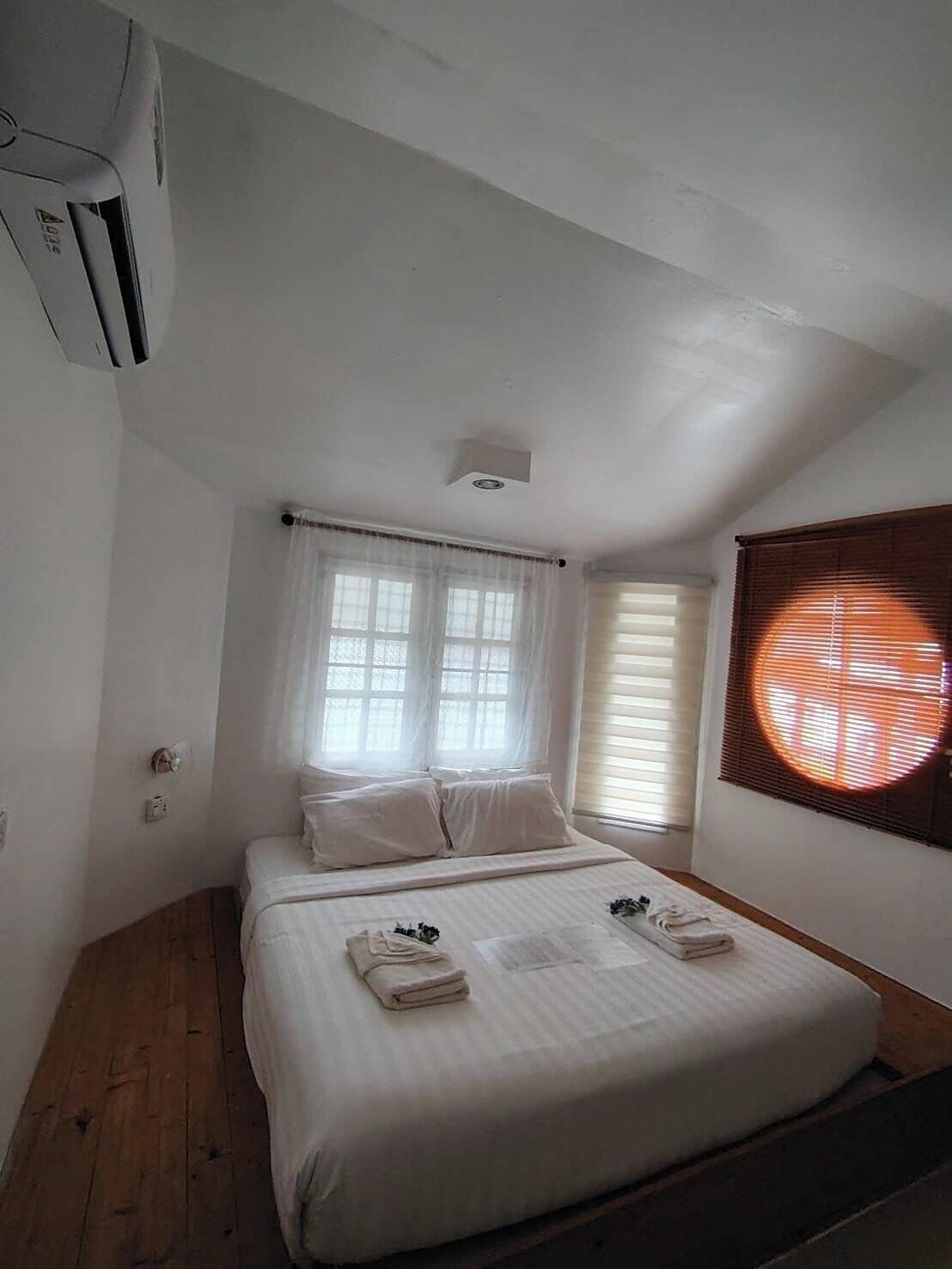 Ein Schlafzimmer mit Bett, Fenster mit Jalousien, Deckenventilator und einer Wand-Klimaanlage.