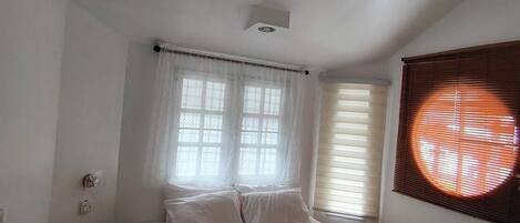 Ein Schlafzimmer mit Bett, Fenster mit Jalousien, Deckenventilator und einer Wand-Klimaanlage.
