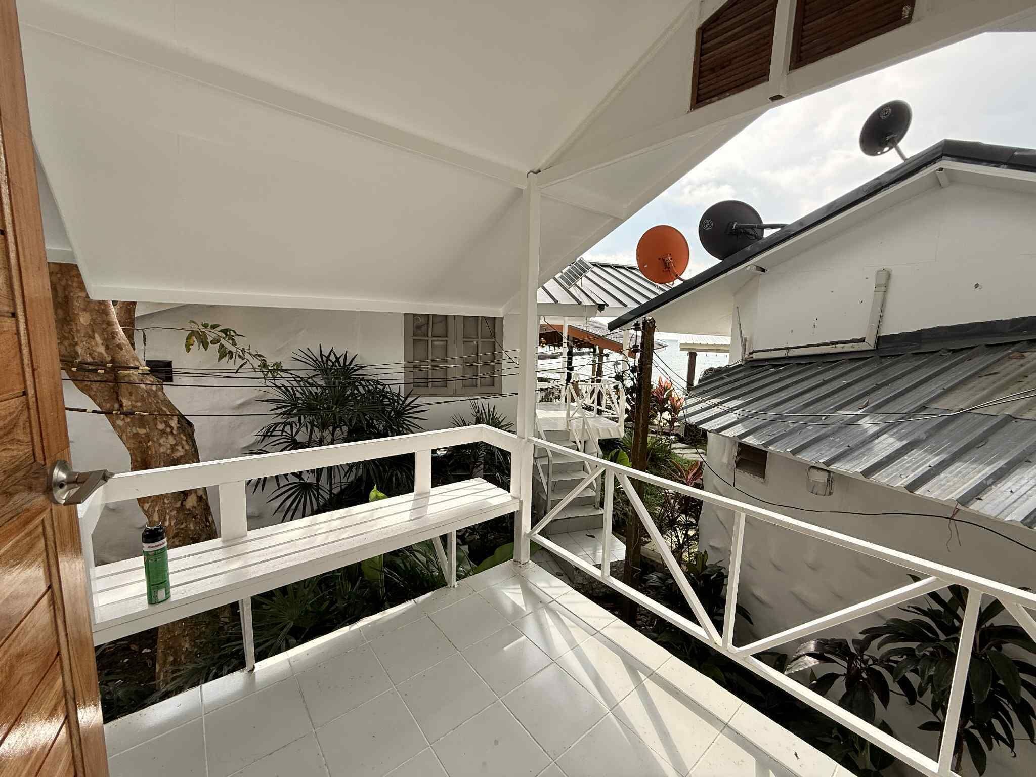 A balcony with a white railing, a wooden door, and a view of the sky and surrounding buildings.